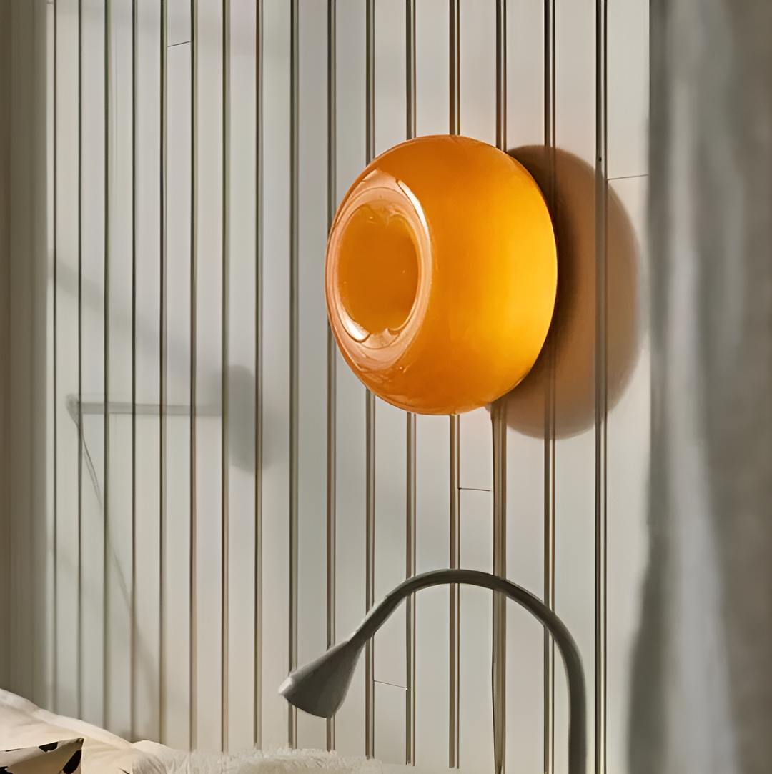 Orange donut-shaped LED lamp for table or wall, made of glass and metal, offering warm glow and whimsical décor touch.