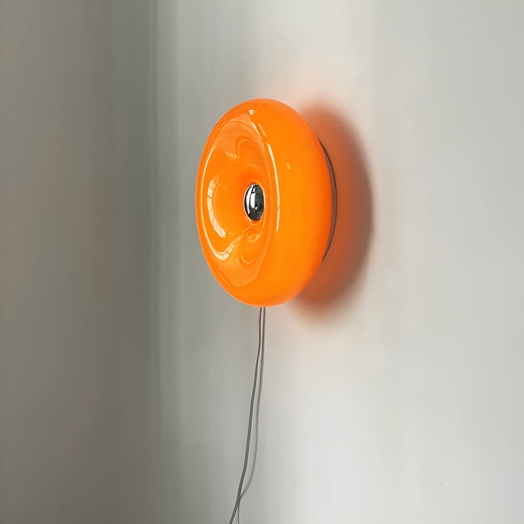 Orange donut-shaped LED lamp for table or wall, made of glass and metal, offering warm glow and whimsical décor touch.