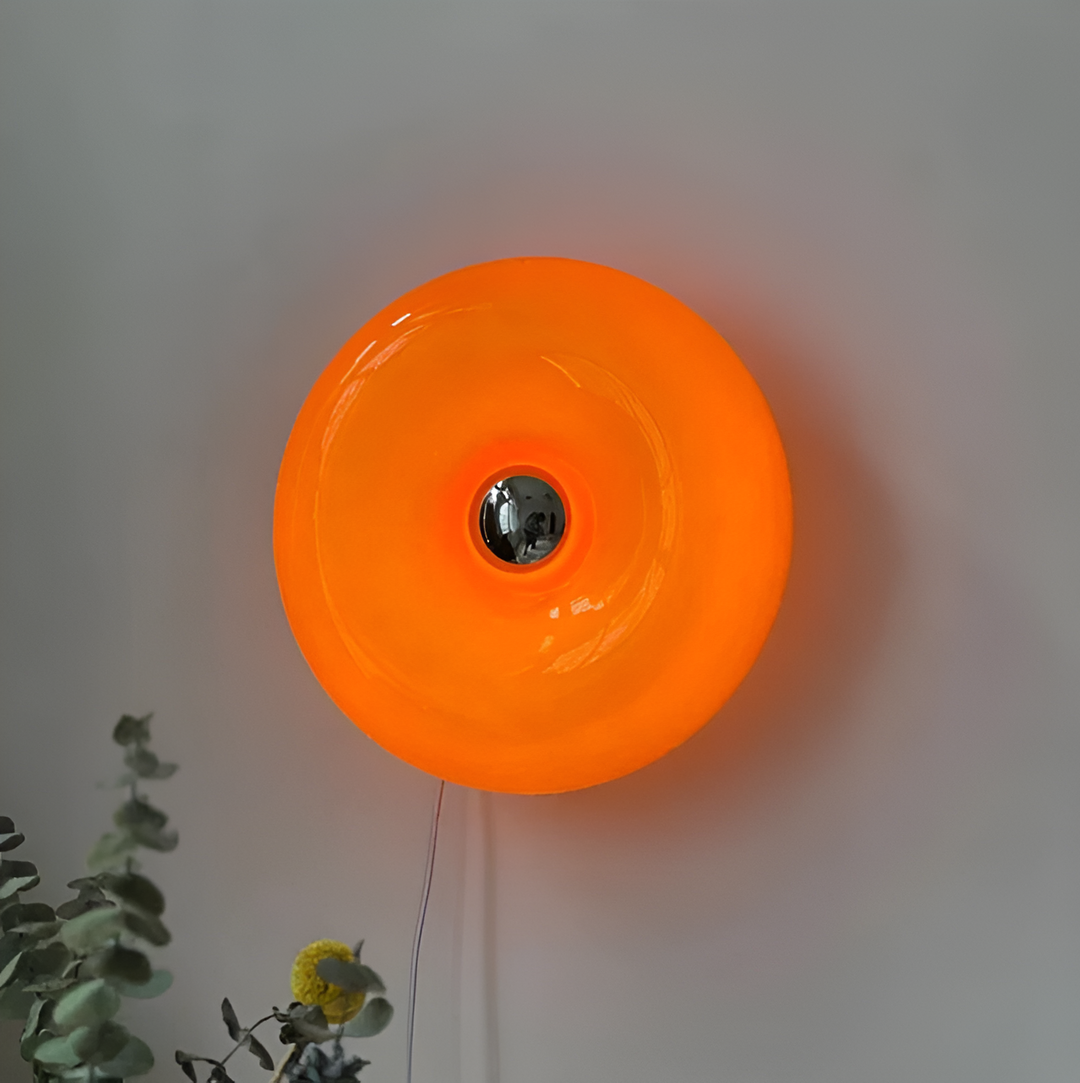 Orange donut-shaped LED lamp for table or wall, made of glass and metal, offering warm glow and whimsical décor touch.