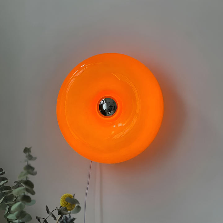 Orange donut-shaped LED lamp for table or wall, made of glass and metal, offering warm glow and whimsical décor touch.