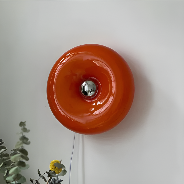 Orange donut-shaped LED lamp for table or wall, made of glass and metal, offering warm glow and whimsical décor touch.